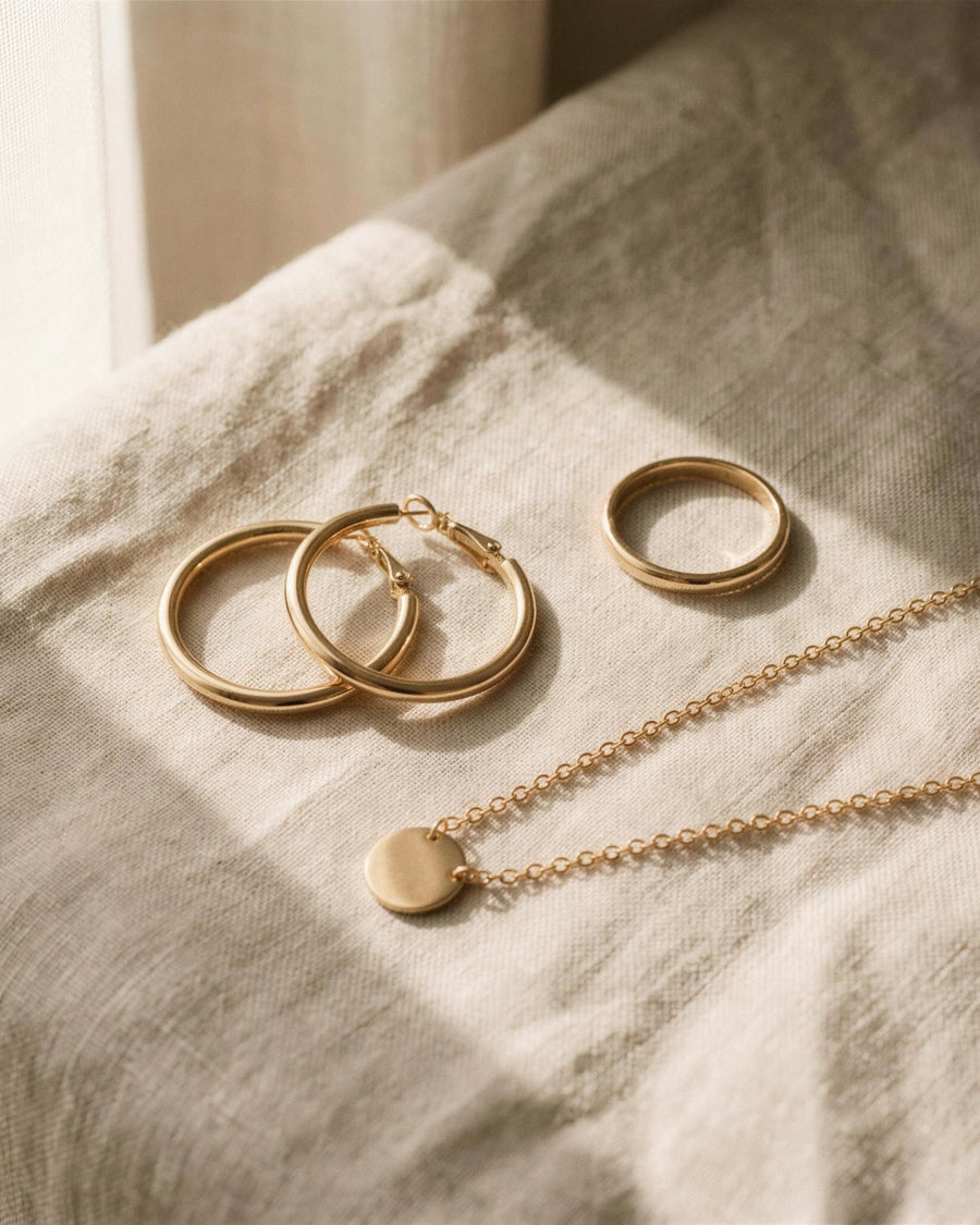 Gold tone hoop earrings, a band ring and a disc pendant necklace on linen