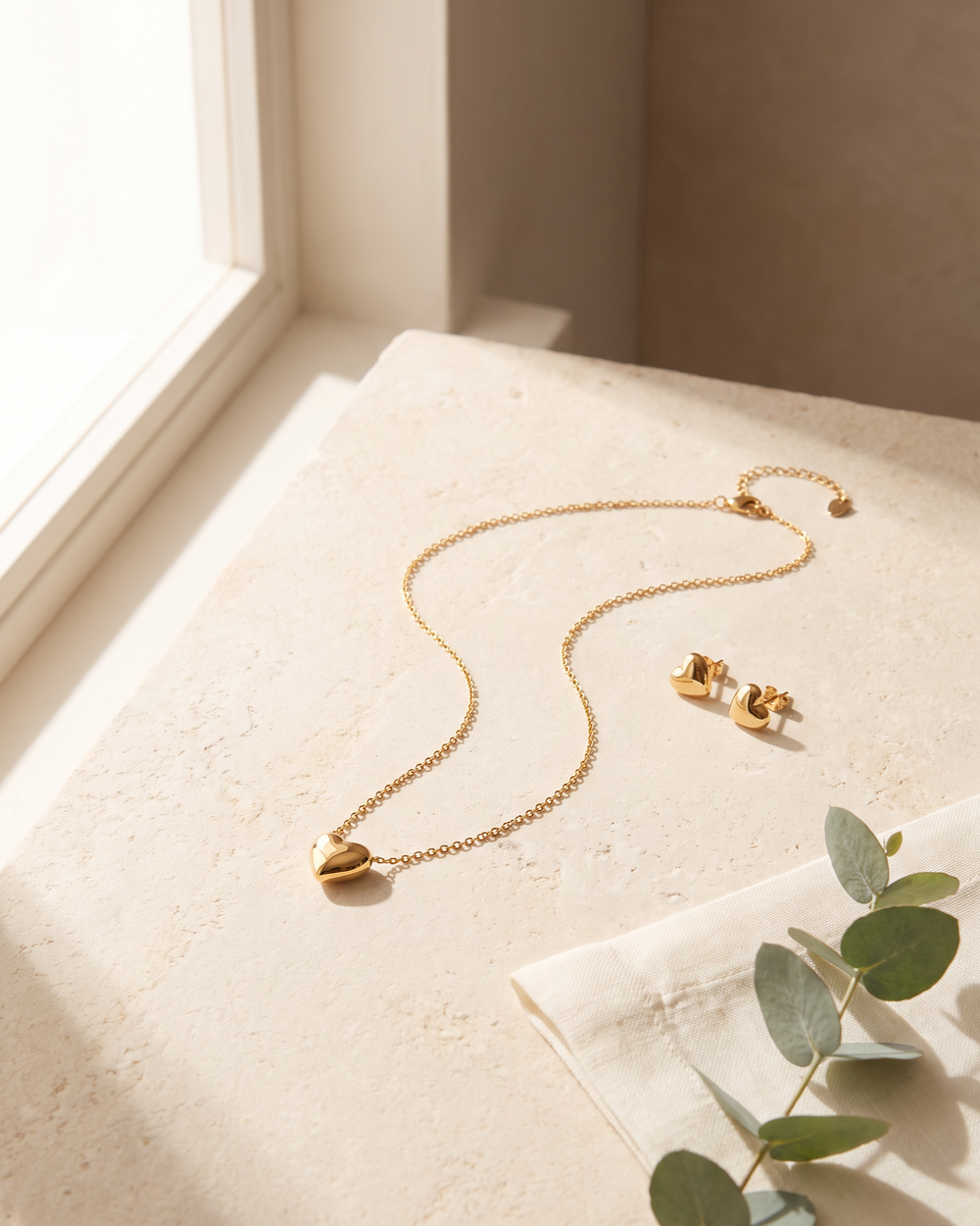Gold tone heart pendant necklace with matching heart stud earrings on pale stone