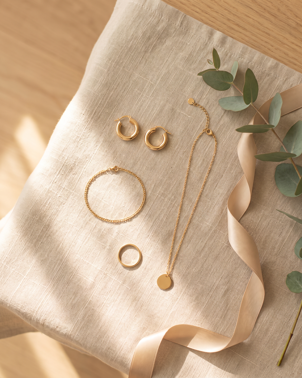 Gold tone hoop earrings, chain bracelet, band ring and pendant necklace laid out on linen