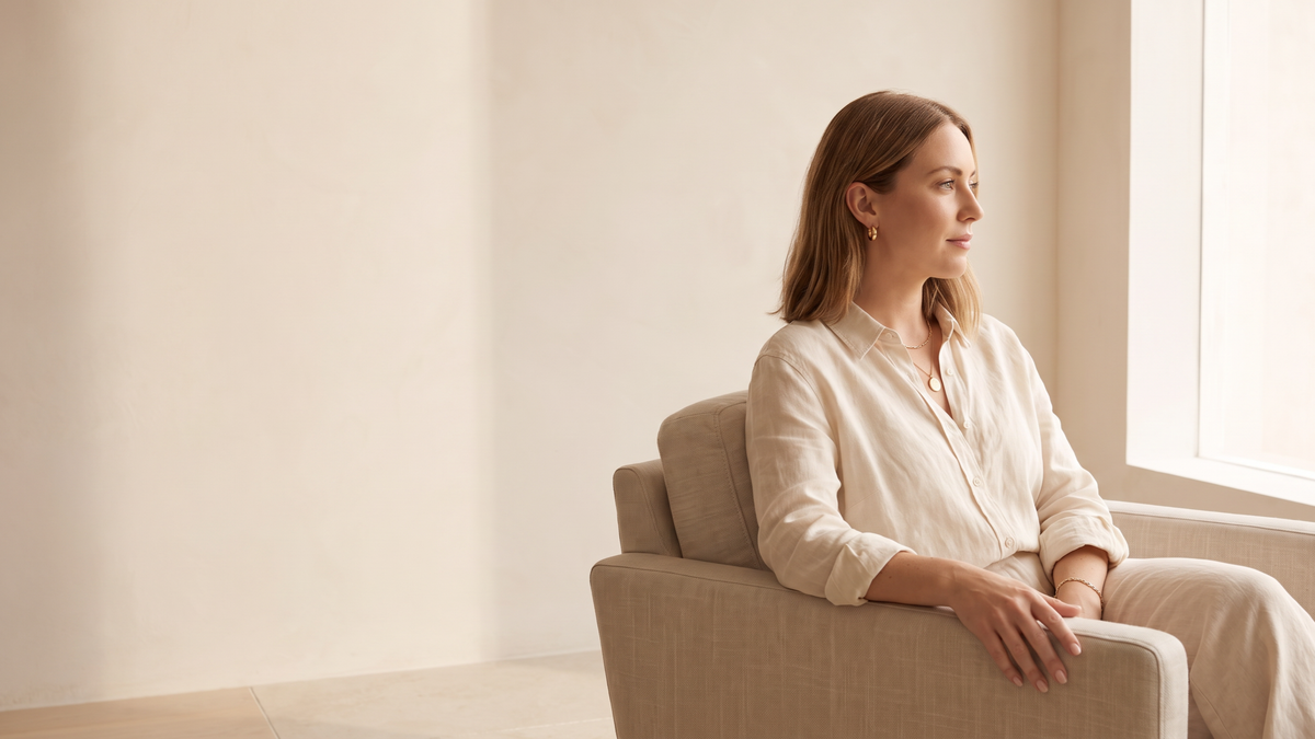 Woman on a linen sofa wearing gold tone hoop earrings, a pendant necklace and a chain bracelet