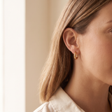 Close-up of a small gold tone hoop earring worn in the ear