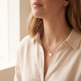Close-up of a thin gold tone chain necklace with a small round pendant