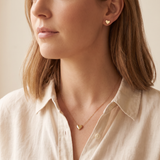 Woman wearing a matching gold tone heart necklace and heart stud earrings