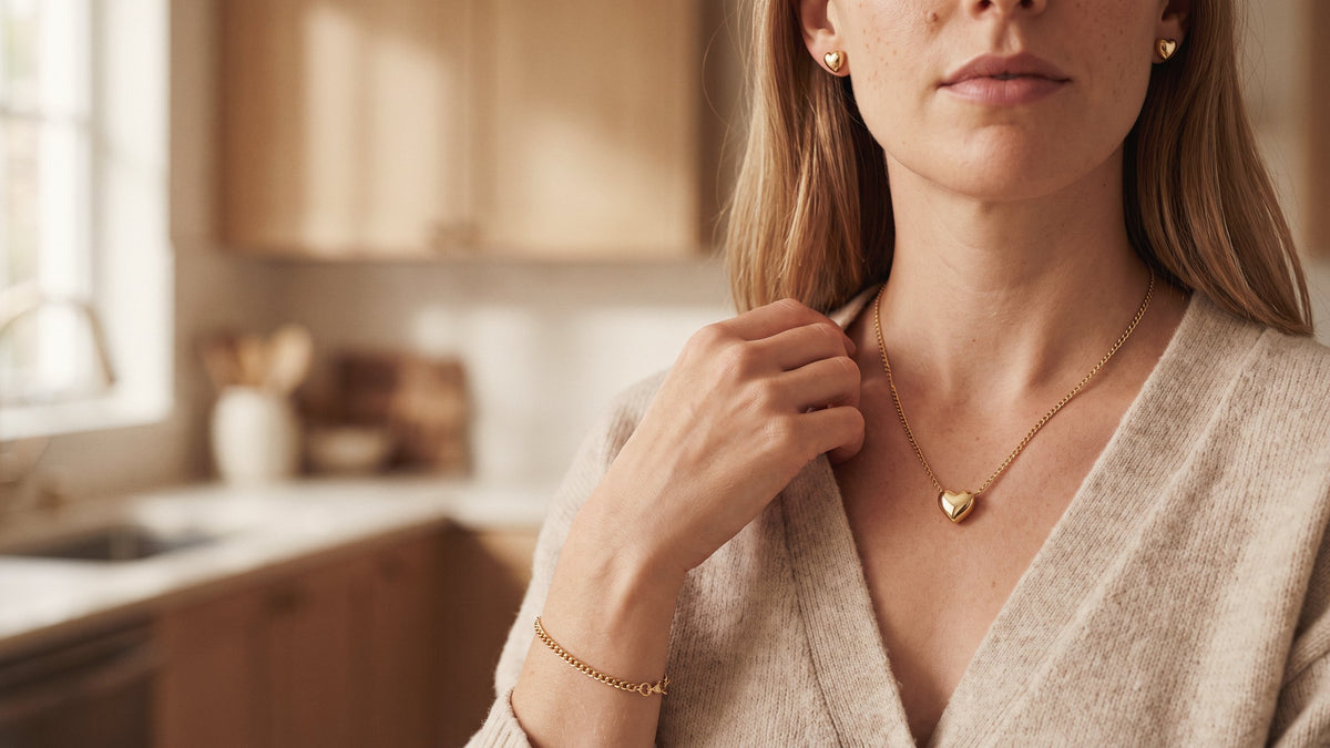 Model in an oatmeal cardigan wearing a gold tone heart necklace, heart stud earrings and a chain bracelet